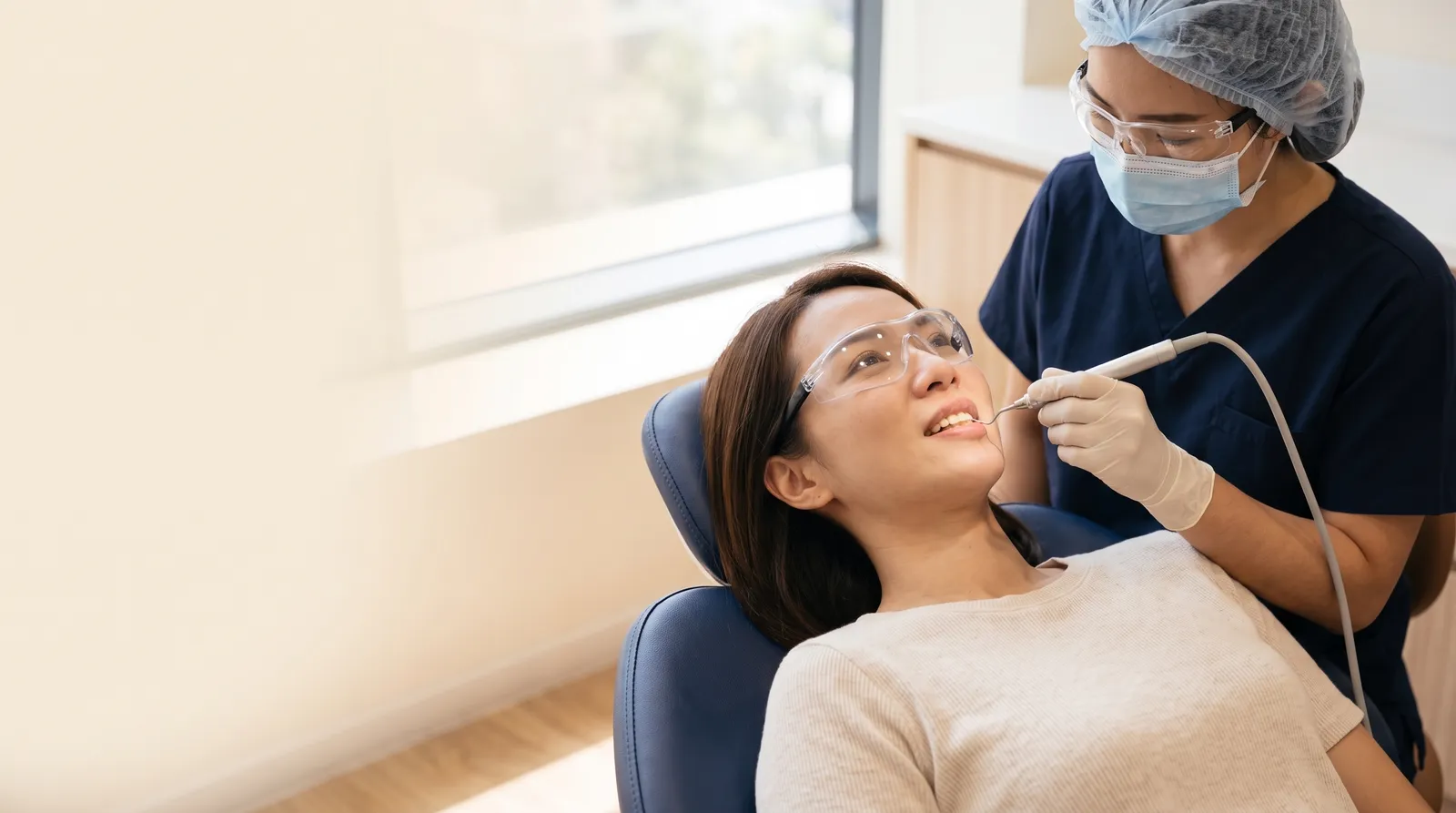 Dental clinician in navy scrubs using an ultrasonic scaler on a relaxed patient in a dental chair